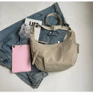 Draufsicht auf beige Halbmond-Umhängetasche mit gewebtem Reißverschluss und Accessoires