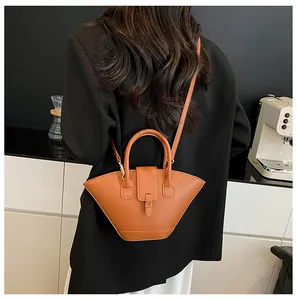 Detail of tan fan-shaped handbag with golden hardware on a model in a black suit jacket