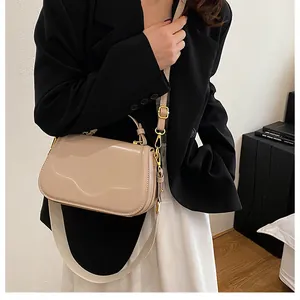 Détail du sac à main en cuir beige poli avec rabat ondulé et fermoir doré porté par mannequin