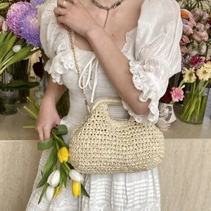 Handmade woven straw beach bag with gold chain strap shown on model in nature