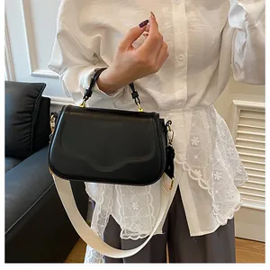 Détail du sac à main noir avec rabat ondulé et large bandoulière en tissu blanc