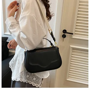 Détail du sac bandoulière en cuir noir avec large sangle en tissu blanc contrasté