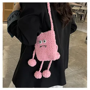 Detail of pink knitted monster crossbody bag featuring decorative legs and fluffy pom-poms