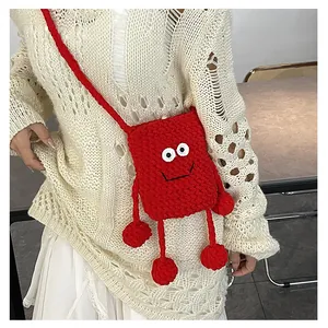 Close-up of a red knitted cartoon mushroom bag with cute eyes and plush pom-poms