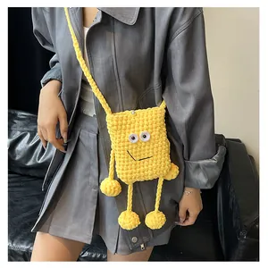 Close-up of handmade yellow knitted crossbody bag featuring a funny cartoon face and limbs