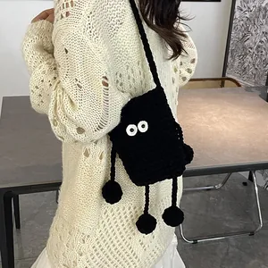 Quirky black knitted monster crossbody bag featuring large eyes and hanging pom-pom legs
