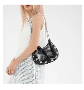 Détail d'un sac demi-lune noir avec clous argentés et chaîne porté par un mannequin femme