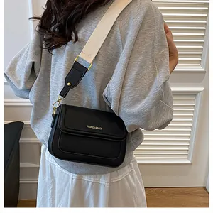 Détail du sac noir à texture litchi avec lettrage doré et large bandoulière crème