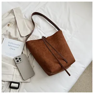 Vue de dessus d'un sac seau en daim marron mat sur fond blanc avec accessoires