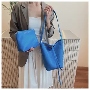 Détail du sac seau en daim bleu et pochette en cuir assortie portés avec un costume