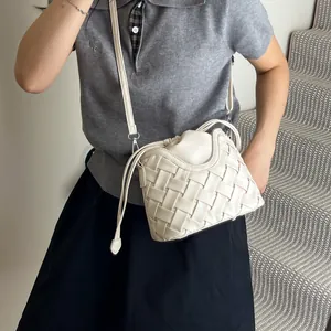 Sac seau tissé beige à la mode avec longue bandoulière présenté dans un cadre de vie extérieur