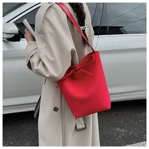 Détail du sac seau rouge mat avec nœud porté sur un trench-coat beige classique