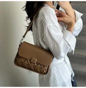 Sac bandoulière en cuir tressé marron porté à l'épaule par un mannequin en extérieur
