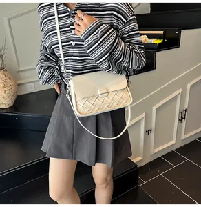Détail du sac bandoulière en cuir tressé beige avec boucle métal porté par le modèle