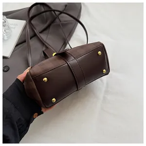 Detalle de la base del bolso a cuadros marrón con pies metálicos dorados y cuero liso