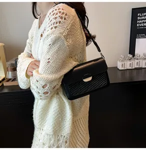 Detail of black shoulder bag with woven flap and silver oval metal buckle on crossbody strap