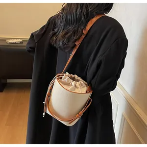 Vista detallada del bolso cubo de lona con ribetes de cuero en contraste y cordón ajustable