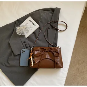 Primer plano de bolso retro marrón con cadena, lazo y colgante sobre un blazer gris