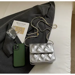 Detalle de bolso acolchado plateado con cadena y móvil mostrando el tamaño mini