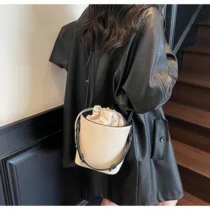 Vista detallada del bolso de cubo crema con correa de cuero negro en un modelo real