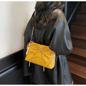 Detalle del bolso amarillo con lazo, textura de cuero y colgante de cuentas de colores