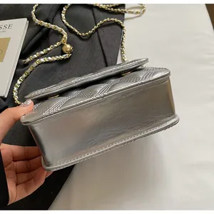 Detalle de la base del bolso acolchado plateado con cadena y adorno de bola dorada