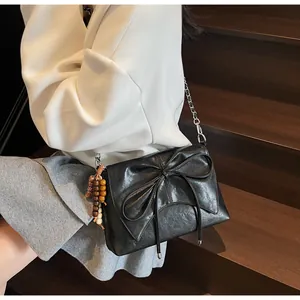 Detalle de bolso negro con lazo grande y colgante de cuentas de madera vintage
