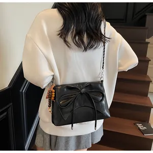 Detalle de bolso bandolera de cuero negro con lazo, cadena y colgante de leopardo