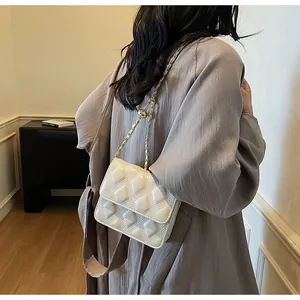Detalle del bolso bandolera acolchado blanco con cadena dorada ajustable llevado por modelo