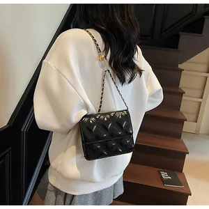 Bolso bandolera acolchado negro con cadena dorada usado en el hombro de la modelo