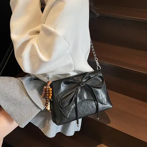 Bolso de hombro negro con lazo grande y colgante de cuentas de madera en una modelo