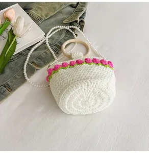 Detalle del bolso tipo cubo tejido a mano con flores rosas de ganchillo y correa de perlas