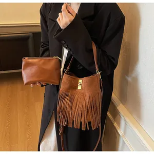 Macro view of brown suede bucket bag featuring long fringe tassels and metal lock closure