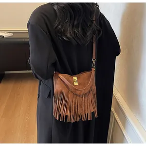 Close-up of a brown suede shoulder bag featuring long fringe and a gold metal twist lock