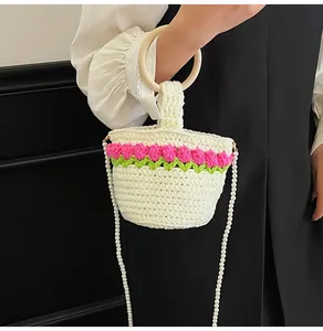 Detalle del bolso de punto con tulipanes rosas, asa de madera y correa de perlas