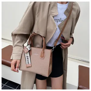 Detail of khaki textured tote with branded strap and adjustable shoulder strap worn by model