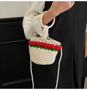 Detalle de bolso tipo cubo tejido a mano en crema con tulipanes rojos y asa de perlas