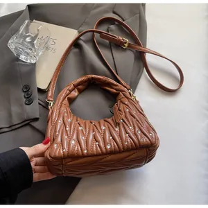 Detalle de bolso marrón plisado con pedrería sobre una chaqueta gris elegante