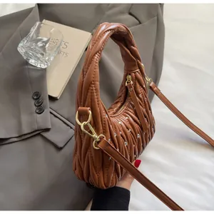 Primer plano del bolso de cuero plisado marrón con pedrería sobre blazer gris