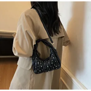 Detalle de bolso plisado negro con remaches decorativos y asa anudada de diseño