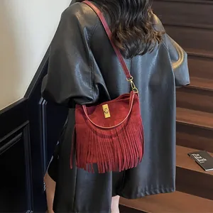 Vintage burgundy suede shoulder bag with tassel fringe and gold clasp on wooden steps