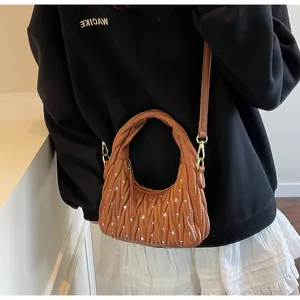 Detalle del bolso de mano plisado color caramelo con pedrería y correa ajustable