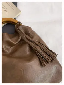 Detalle de bolso cubo de cuero marrón con asa de madera y flecos decorativos largos