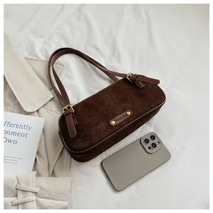 Detalle de bolso baguette de ante con logo metálico y correa de cuero marrón