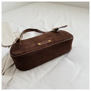 Detalle del bolso de hombro en ante marrón oscuro con acabados dorados sobre tela blanca