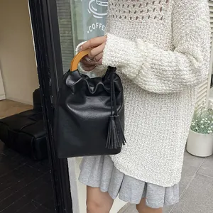 Bolso saco negro retro con textura vintage, asa de madera y detalles de borlas