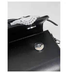 Detalle de cierre magnético plateado en bolso de cuero negro con encaje blanco fino