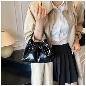 Primer plano de bolso plisado en charol negro brillante con modelo en abrigo beige