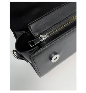 Detalle de bolso de cuero negro mate con cremallera plateada y cierre magnético de presión