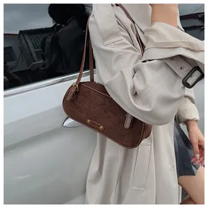 Detalle de bolso baguette marrón mate con placa metálica dorada sobre un abrigo